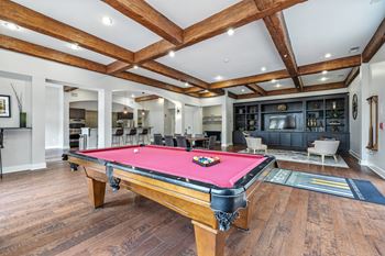 A pool table in a room with wooden floors and a high ceiling.